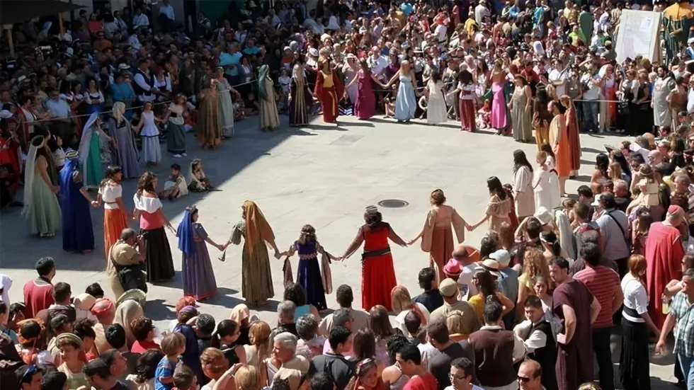 Adultos con trajes tradicionales formando un gran corro en una plaza, el baile folklórico del que descienden las rondas.