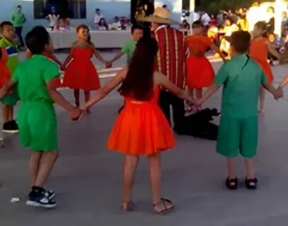 Niños con vestuario de colores bailando en corro Naranja Dulce, Limón Partido en el patio.